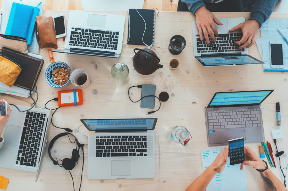 Overhead view of a work table with laptops, phones and notebooks