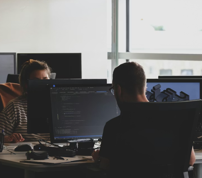Two people coding at their monitors in an office