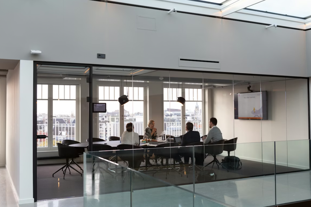 A glass-walled meeting room with a team working around a table